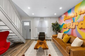 A modern living room with a staircase, a red chair, a brown leather sofa, and a colorful mural on the wall. - Retro SoCo GetawayTownhome! (Austin)