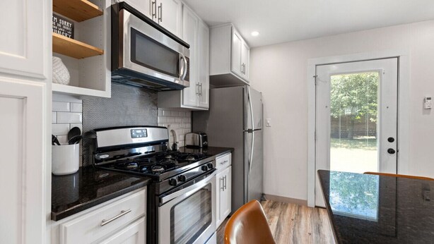 A modern kitchen with stainless steel appliances, white cabinetry, and a wooden dining table. - Retro SoCo GetawayTownhome! (Austin)