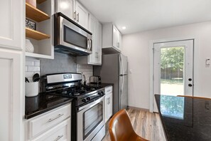 A modern kitchen with stainless steel appliances, white cabinetry, and a wooden dining table. - Retro SoCo GetawayTownhome! (Austin)