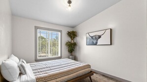 A bedroom with a bed, a window with blinds, a wall-mounted picture, and a plant. - Retro SoCo GetawayTownhome! (Austin)