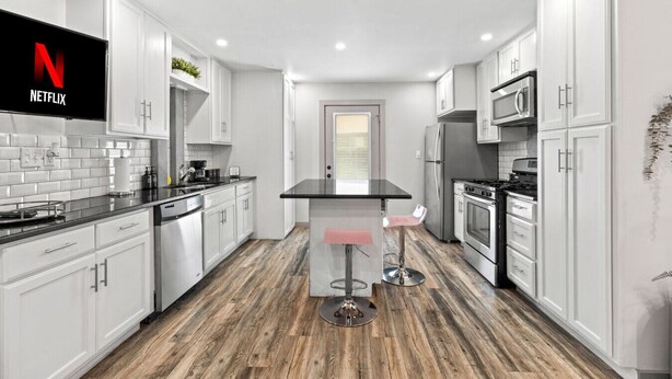 A modern kitchen with white cabinetry, a central island, a microwave, and a refrigerator. - Pink Palace SoCo Dream Townhome! (Austin)