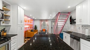 A modern kitchen with a central island, white cabinetry, and a pink staircase. - Pink Palace SoCo Dream Townhome! (Austin)