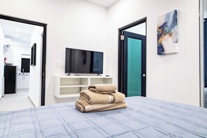 A hotel room with a bed, a television on a stand, a painting on the wall, and a bathroom visible through an open door.