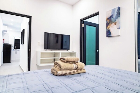 Une chambre d’hôtel avec un lit, un téléviseur posé sur un meuble, un tableau accroché au mur et une salle de bain visible à travers une porte ouverte.
