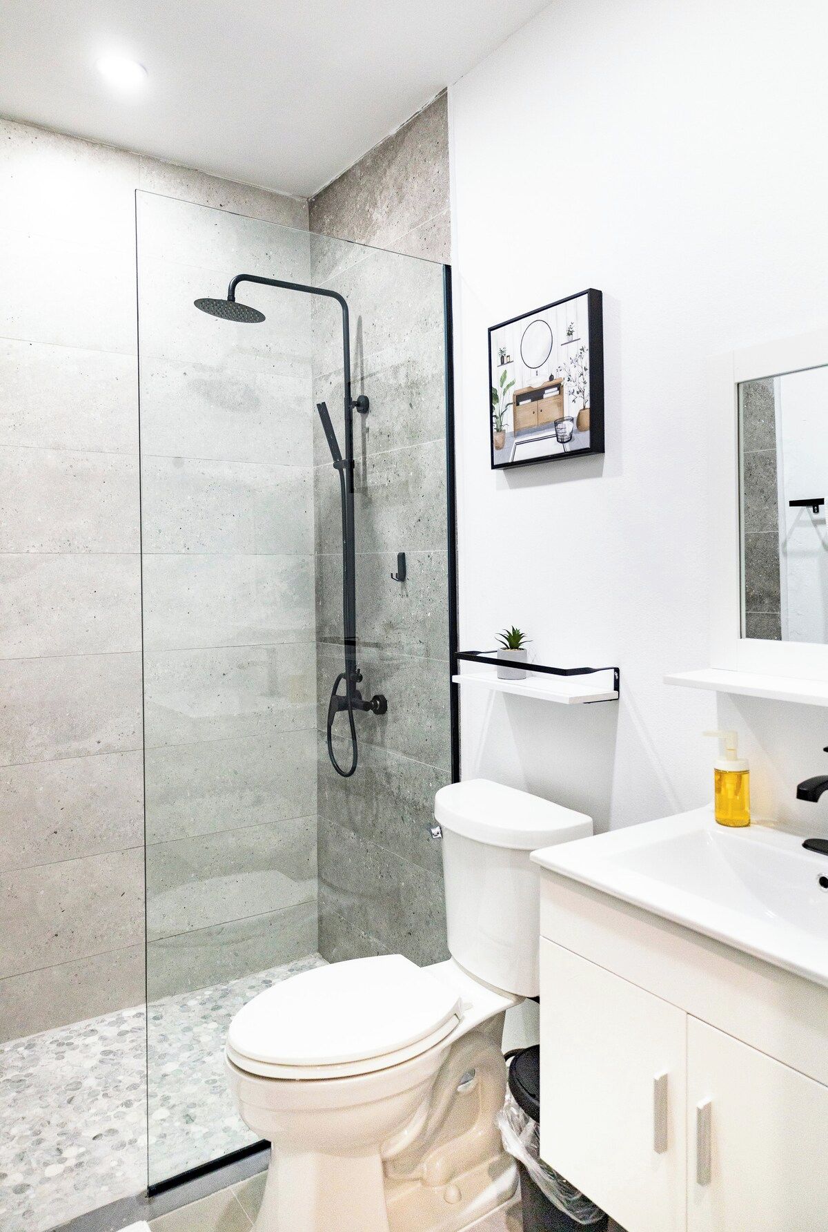 A modern bathroom with a glass-enclosed shower, a toilet, and a vanity with a mirror.