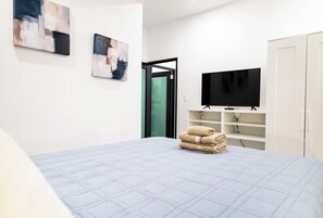 A hotel room with a bed, a television, a wardrobe, and abstract art on the wall.