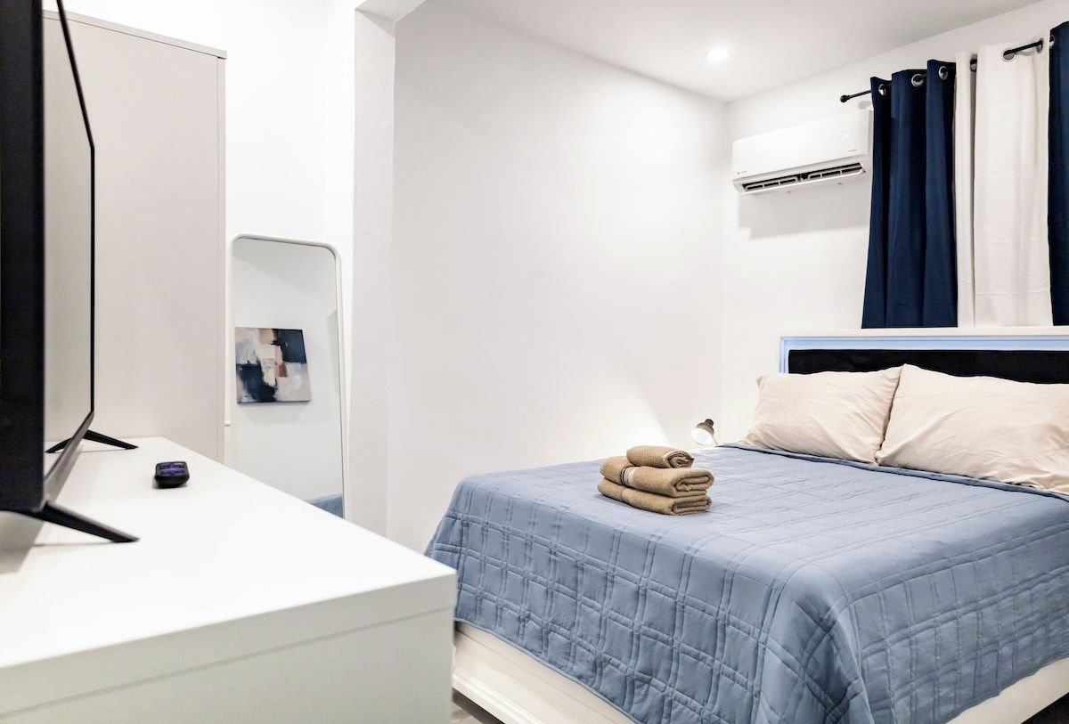 A bedroom with a bed, a bedside table, a mirror, and a wall-mounted air conditioner.