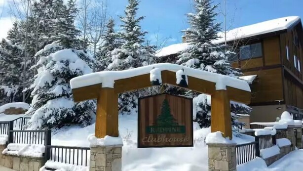 Una entrada cubierta de nieve con un arco de madera y un letrero que dice "Clubhouse".