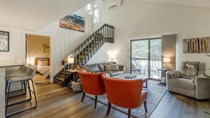 Amplia sala de estar con escalera, zona de comedor con sillas color naranja y un sofá.