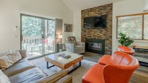 Una sala de estar con chimenea de piedra, televisor montado en la pared, un sofá y una mesa de centro.