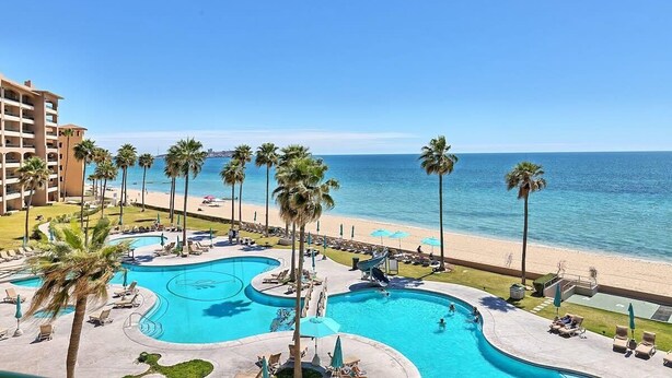 A resort with a large pool area, palm trees, and a beach view.