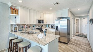 A modern kitchen with white cabinets, stainless steel appliances, and a marble island with bar stools.