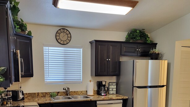 A kitchen with dark cabinets, a stainless steel refrigerator, a granite countertop, and two wooden chairs. - Charming 2BD / 1 BA farmhouse on 2.5 acres w/mountain views in fabulous Glendale (Glendale)