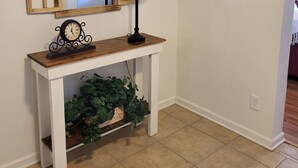 A hallway with a wooden console table, a mirror with a decorative frame, a clock, a lamp, a potted plant, and a framed artwork on the wall. - Charming 2BD / 1 BA farmhouse on 2.5 acres w/mountain views in fabulous Glendale (Glendale)