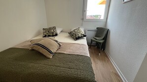 A small, neatly arranged bedroom with a bed, pillows, a chair, and a window. - Seafront T3 Apartment in Arcachon with Secure Parking (Arcachon)