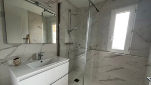 A modern bathroom with a marble backsplash, a white vanity, a glass shower enclosure, and a window providing natural light. - Seafront T3 Apartment in Arcachon with Secure Parking (Arcachon)