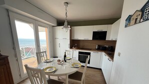 A kitchen with white cabinets, a dining table with chairs, and a view of the ocean through a sliding door. - Seafront T3 Apartment in Arcachon with Secure Parking (Arcachon)