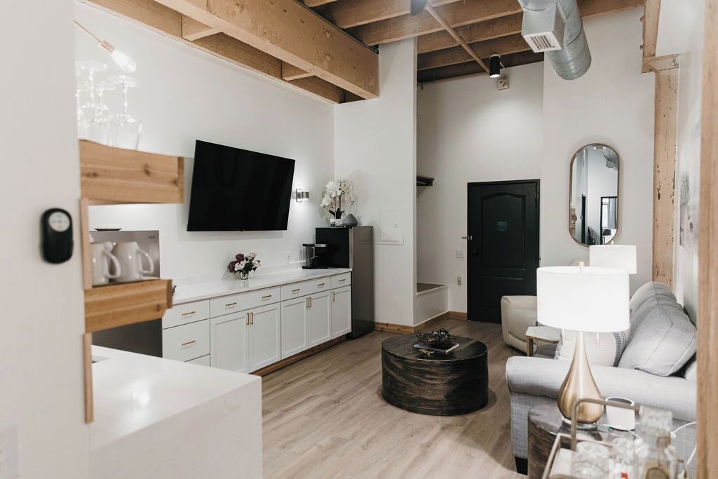 A modern living room with a flat-screen TV, a sofa, a coffee table, and a dining area with a kitchen counter.