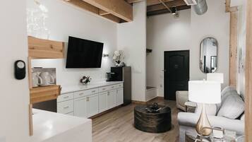 A modern living room with a flat-screen TV, a sofa, a coffee table, and a dining area with a kitchen counter.