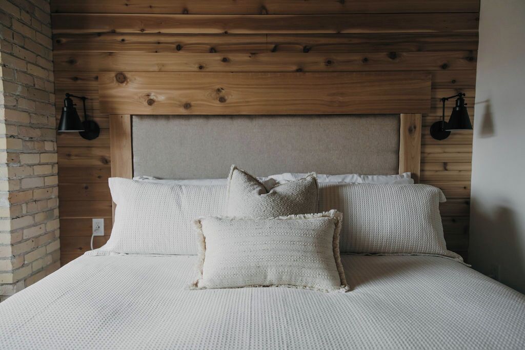 A bedroom with a wooden headboard, two white pillows, and a textured bedspread.