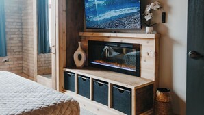 Een kamer met een bed, een televisie bevestigd aan een houten muur, een openhaard en een deur.