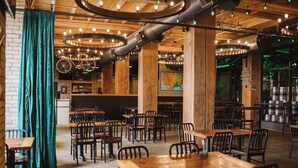 Een restaurantinterieur met houten tafels en stoelen, een bar en een grote kaart aan de muur.