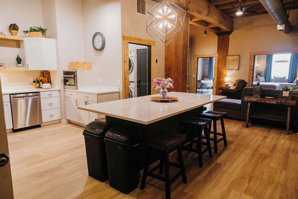 A modern kitchen with a central island, bar stools, and a dining area with a table and chairs.