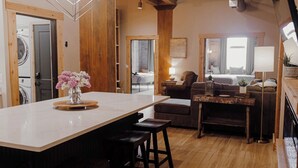 A spacious kitchen with a large island, wooden beams, and a view into the dining area. - Dockside Suites | The Brix | Pool in Canal Park! (Duluth)