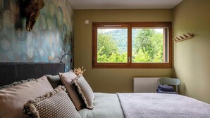 Een slaapkamer met een bed, een raam met uitzicht op groen, een radiator en een wandplank.