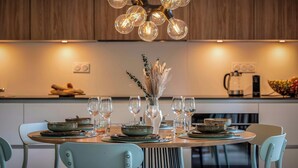 Een moderne eetruimte met een ronde tafel voor vier personen, omringd door lichtblauwe stoelen. Een bijzondere kroonluchter met meerdere bolvormige lampen hangt erboven.