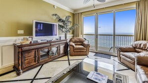 Una sala de estar con un televisor grande, sillones de cuero, un mueble de madera y vista al océano a través de amplios ventanales.