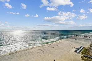 Une plage avec une jetée qui s’avance dans l’océan, une plage de sable et un ciel dégagé.