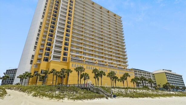 A high-rise hotel with multiple balconies, a sandy beach in front, and palm trees. - Sterling Reef 202 - 2nd Floor w/Uninterrupted Gulf View!  Free Fun! (Panama City Beach)