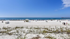 A beach with white sand, a few umbrellas, and a small structure. - Sterling Reef 202 - 2nd Floor w/Uninterrupted Gulf View!  Free Fun! (Panama City Beach)