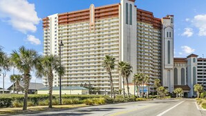 A multi-story hotel with a central tower, palm trees, and a clear sky.