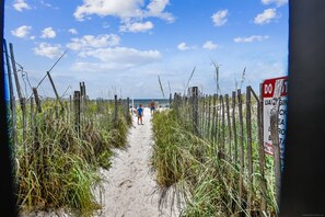 Un sentier de plage sablonneux bordé d’une clôture en bois et agrémenté d’un panneau indiquant « Entrée interdite ».
