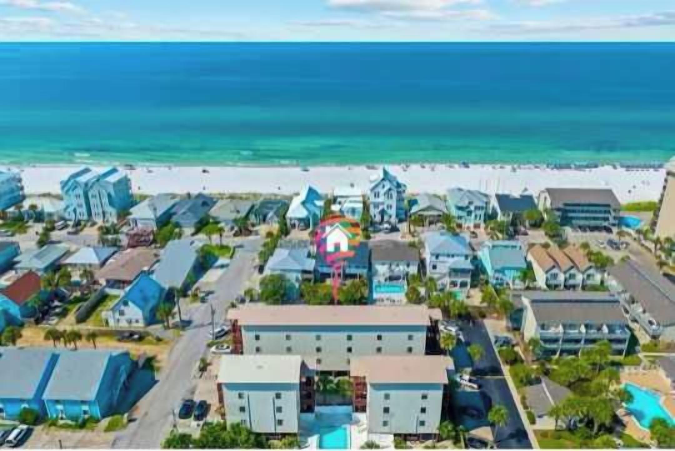 A coastal hotel with multiple buildings, a beach in the background, and a clear sky.