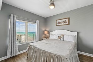 Quarto com cama, janela com cortinas, mesa de cabeceira com abajur e um letreiro na parede.