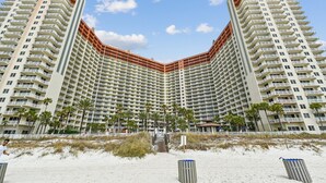 A high-rise hotel with multiple balconies, a beach in the foreground, and a clear sky.