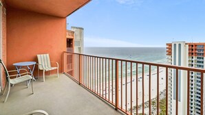 Ein Balkon mit Blick auf Meer und Strand, ein Tisch, ein Stuhl und ein kleines Fenster.