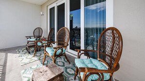 A balcony with wicker chairs and a small table, large sliding glass doors, and a view of the cityscape.