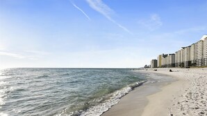 A beach with a sandy shore, a pier extending into the water, and high-rise buildings along the coastline.