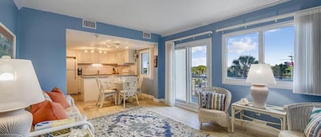 A spacious living room with a large window, a dining area, and a kitchen.