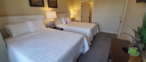 A hotel room with two beds, a nightstand, a lamp, a door, and a plant.