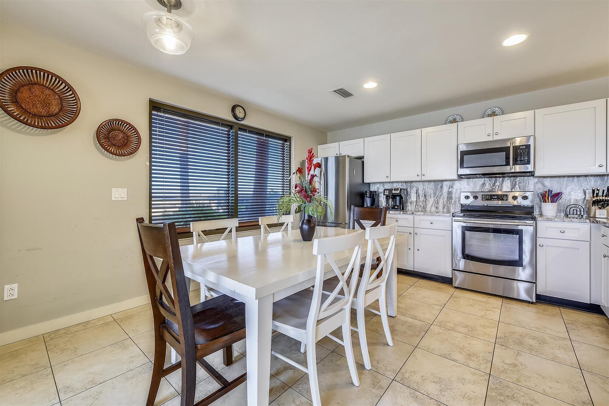 Una cocina moderna con armarios blancos, electrodomésticos de acero inoxidable y una zona de comedor con mesa y sillas blancas.
