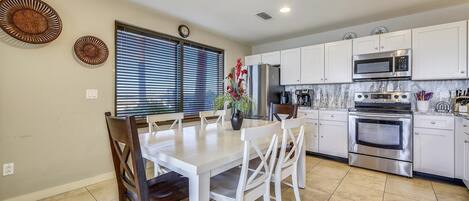 Una cocina moderna con armarios blancos, electrodomésticos de acero inoxidable y una zona de comedor con mesa y sillas blancas.