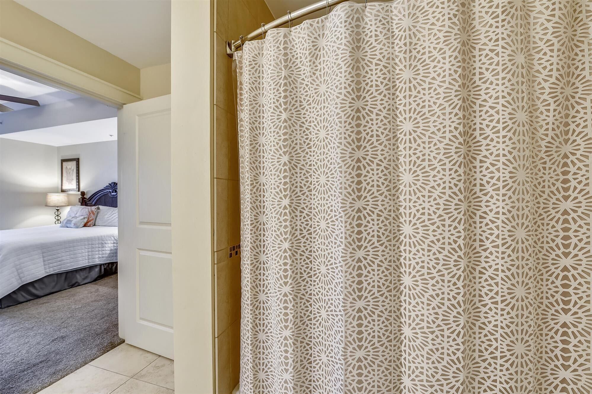 A hotel room with a bed, a nightstand, a lamp, and a patterned curtain.