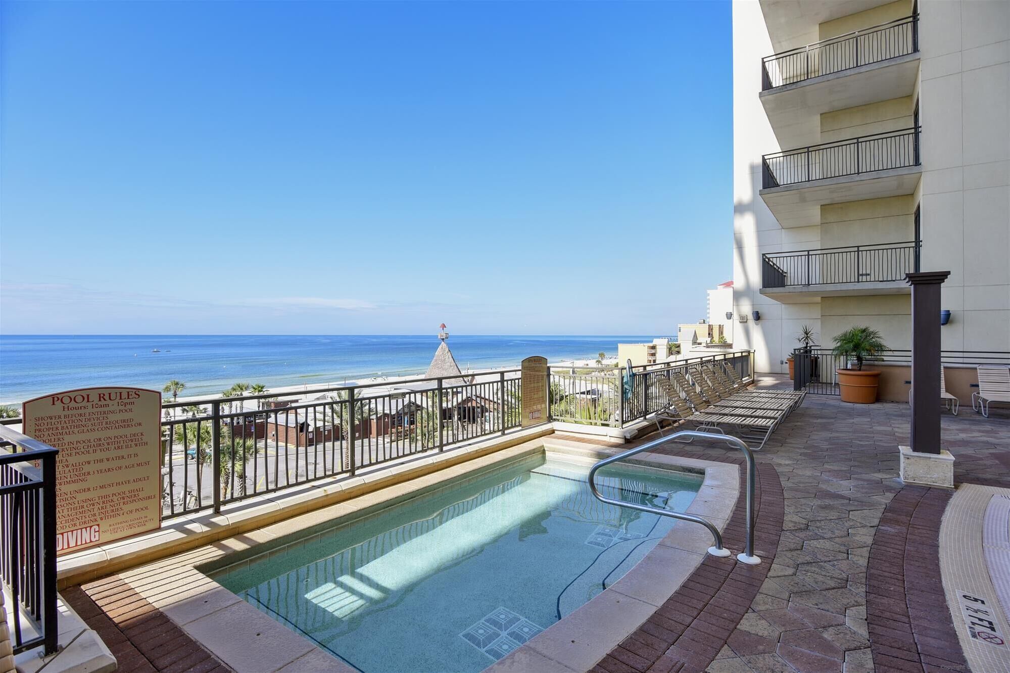 A pool area with a view of the ocean, a lifeguard tower, and a building with balconies.