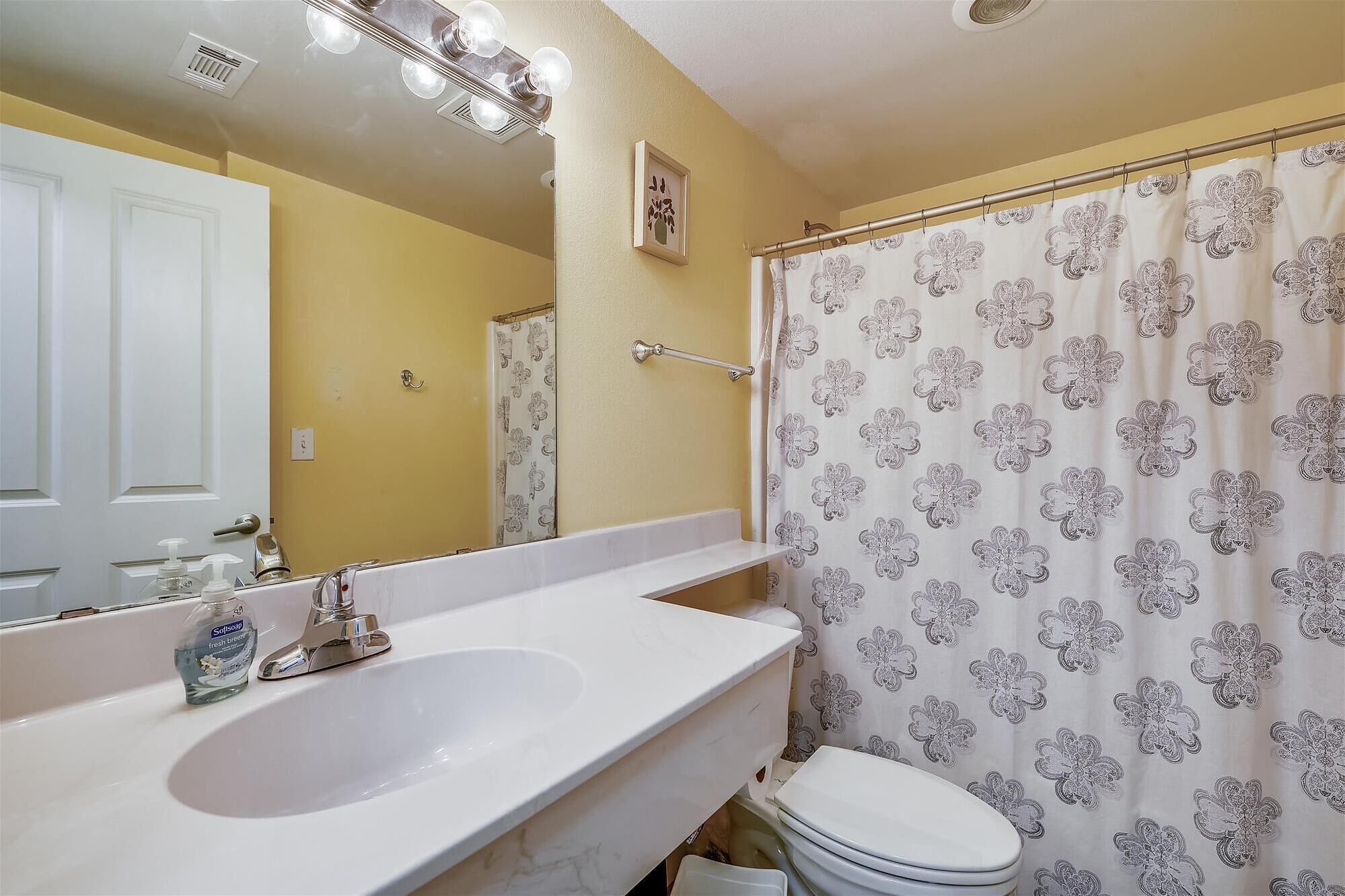 Un baño con lavamanos blanco, inodoro y cortina de ducha con estampado floral.