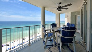 Varanda com mesa e cadeiras, ventilador de teto e vista para a praia e o oceano.